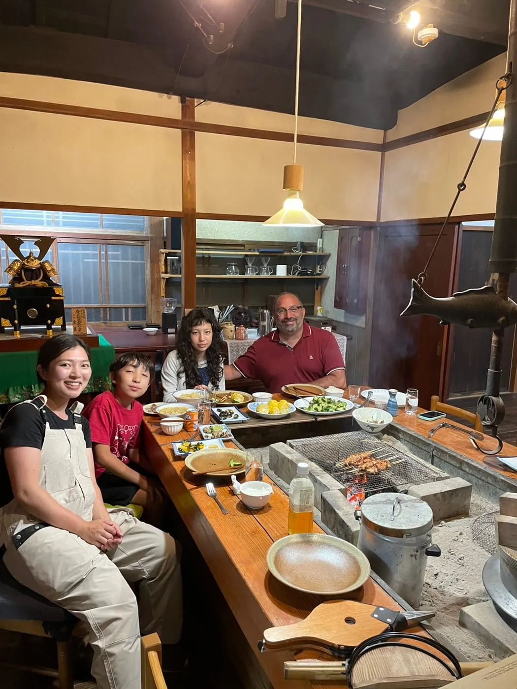 A family of four smiling around the irori hearth